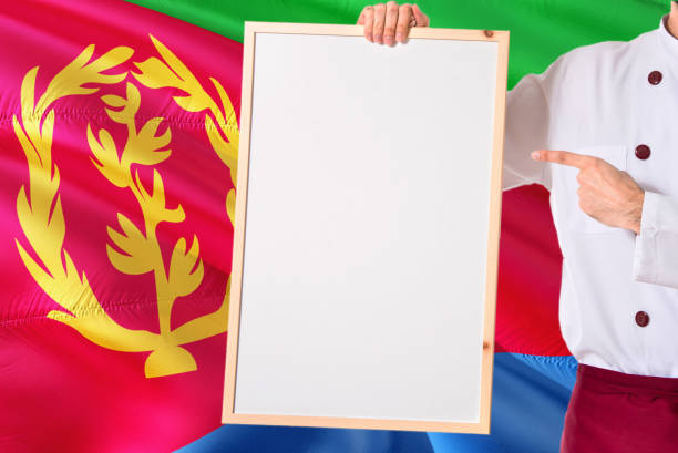 Eritrean Chef holding blank whiteboard menu on Eritrea flag background. Cook wearing uniform pointing space for text.