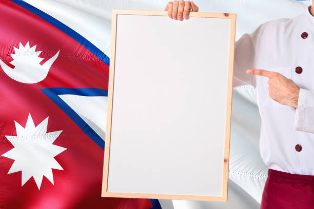 Nepalese Chef holding blank whiteboard menu on Nepal flag background. Cook wearing uniform pointing space for text.