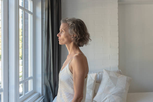 istock Middle aged woman with grey hair looking out window 1132209203