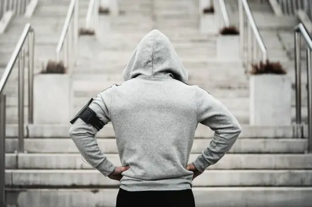 Rear view of hooded sports man about to run upstairs