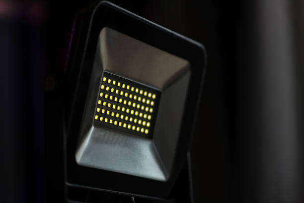 A rectangular diode spotlight of gray color in a dark room illuminates with yellow light. Blurred background