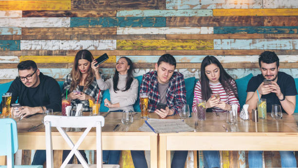 grupo de amigos que usam o smartphone no restaurante rústico-povos novos do hipster viciados pelo telefone móvel na comunidade social da rede - text messaging mobile phone teenagers only people - fotografias e filmes do acervo