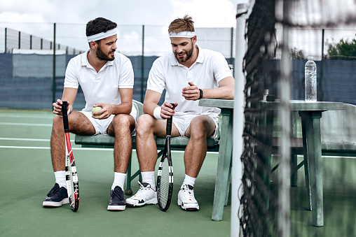 Handsome tennis players relaxing and discussing the match on the court