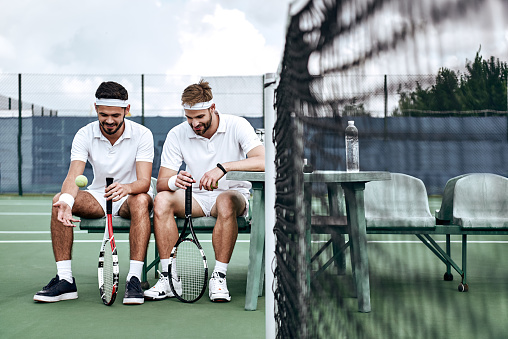 Tennis players are sitting on the bench with the equipment waiting for the match