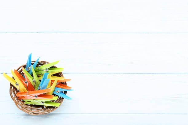 Colorful plastic clothespins in basket on wooden table