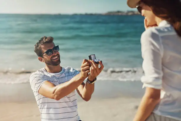 Cropped shot of a young man proposing to his girlfriend at the beach on a summer’s day