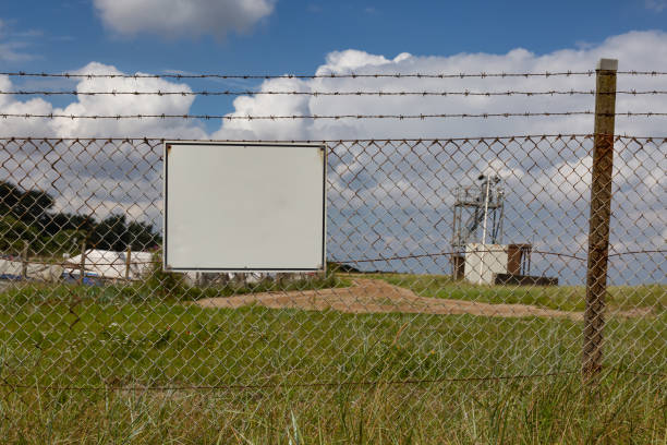 Blank sign on a fence with barbed wire White sign at a barrier barbed wire wire factory sky stock pictures, royalty-free photos & images