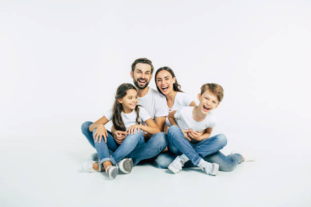 美麗而快樂的微笑的年輕家庭在白色 t恤擁抱和有一個有趣的時間在一起, 而坐在地板上, 看著相機。 - 家庭 圖片 個照片及圖片檔