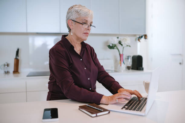 istock Beautiful senior woman using laptop computer at home, browsing internet. Elderly lady typing on computer keyboard and surfing the net 1132220028