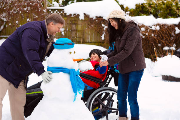 겨울 동안 가족과 함께 눈사람을 만드는 휠체어 장애인 소년 스톡 사진