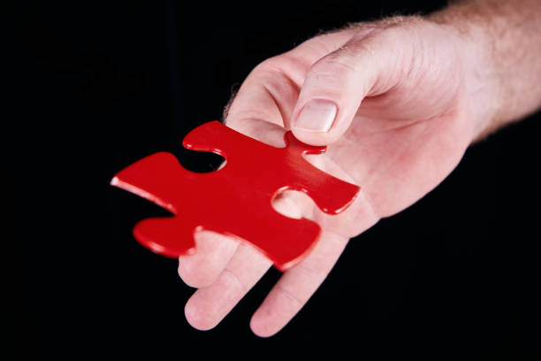 istock Hand holds out single jigsaw piece against black 1132224140