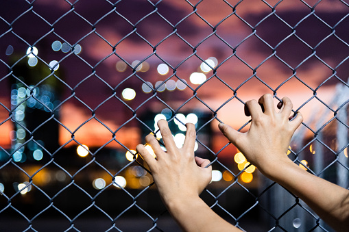 Human hand holding on wire fence at night.