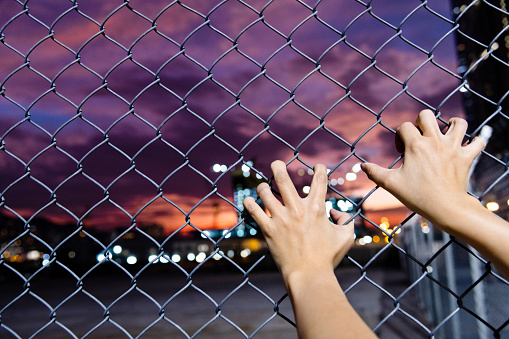 Human hand holding on wire fence at night.
