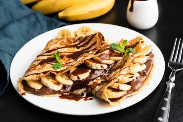 Tasty crepe with hazelnut chocolate spread and banana on white plate