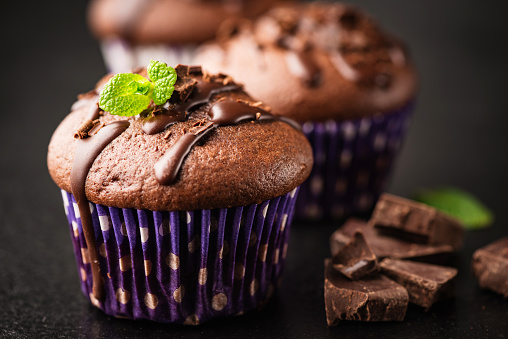 Tasty chocolate muffins closeup view. Chocolate cakes or cupcakes with ganache and mint leaf