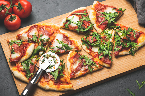Pizza or flatbread with arugula, salami, cheese sliced on wooden cutting pizza board