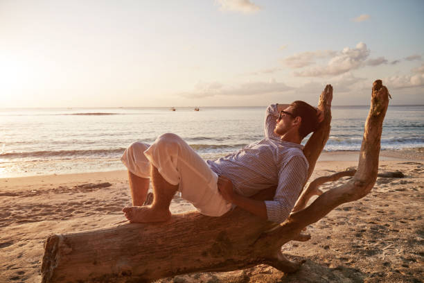 istock Modern man posing on the wooden stump on the sandy beach. 1132236995