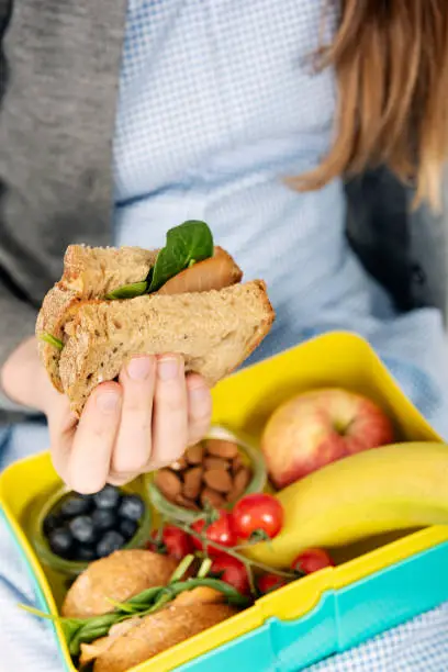School girl opening her lunchbox that contains a healthy mix of food for a healthy school lunch such as, wholemeal bread sandwich, smoked salmon, salad leaves, fruits and nuts. Colour, vertical with some copy space. Please see my other pictures in this series illustrating good/bad concepts.
