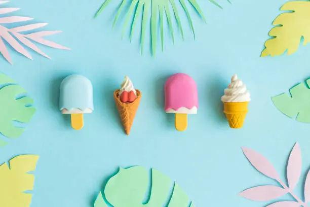 Photo of Ice cream on stick and in wafer cone with multicolored origami tropical leaves abstract on blue.