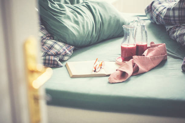 Crumpled bedding with fresh pink fruit smoothies and book for a relaxing day