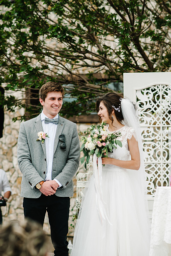 Feliz novia y el novio de pie después de la ceremonia de boda bajo el arco decorado con flores y vegetación en la zona de banquetes del patio trasero. novios recién casados. photo