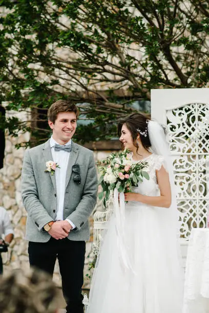 Photo of Happy bride and groom standing after wedding ceremony under the arch decorated with flowers and greenery in the backyard banquet area. couple newlyweds.