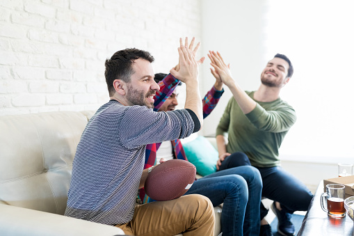 Male fans celebrating score and giving high five while watching American football at home