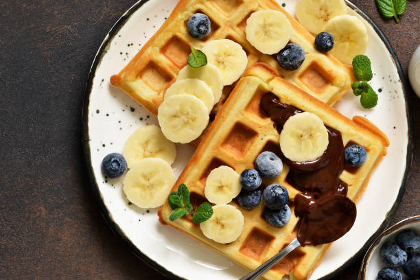 istock Breakfast time. Homemade waffles with banana, blueberry and chocolate spread on a kitchen table. 1132258655