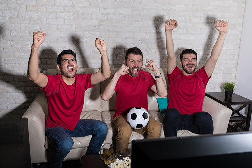 Joyful fans screaming while watching soccer match on TV at home