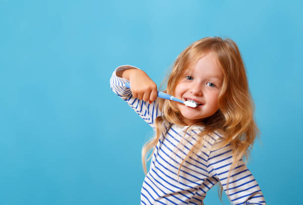 une petite fille en pyjama rayé se brosse les dents avec une brosse à dents. le concept d'hygiène quotidienne. isolé sur un fond bleu - hygiene dental hygiene human teeth child photos et images de collection