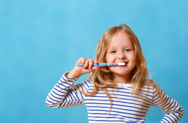 縞模様のパジャマの小さな女の子が歯ブラシで歯磨きをしている。毎日の衛生の概念。青い背景に分離 - child brushing human teeth brushing teeth ストックフォトと画像