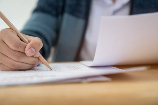 istock Education test concept : Hands with blue pen over application form, Students taking exams, writing examination room with undergraduate inside. Student sitting learning lessons doing final in classroom 1132263982