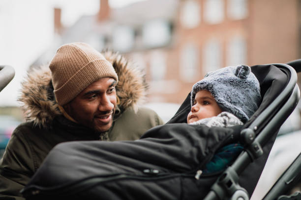 Checking Up on His Baby Son Young Father crouching down to check up on his baby son sitting in a stroller. He is wearing warm clothing and is smiling at his son. baby stroller winter stock pictures, royalty-free photos & images