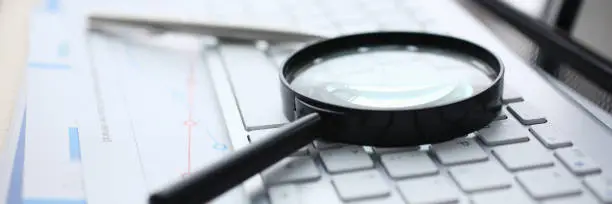 Magnifying glass lies on white keyboard on desk in office table workplace closeup.