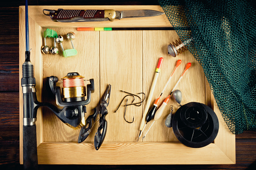 Fishing tackle - fishing, hooks, fishing line and floats, fishing rod with a reel, net, knife and other tools on a wooden background, in a frame. Still life. View from above.