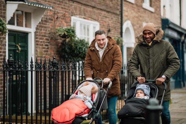 Male Friends Out with Their Babies in Tynemouth, UK Two male friends are out in Tynemouth, North East UK. They are walking on a sidewalk and pushing their baby sons in strollers. They are wearing warm clothing. pushchair stock pictures, royalty-free photos & images