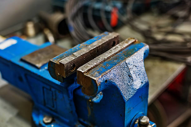 Blue old vise mounted on a workbench in a workshop or carpentry shop. Device for clamping and holding objects and parts.