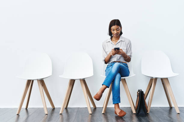 Sending a quick text before I go for the interview Full length studio shot of an attractive young businesswoman sitting down on a chair and using her cellphone cross legged stock pictures, royalty-free photos & images