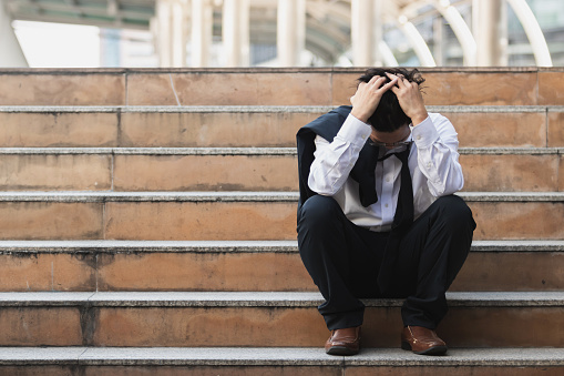 Malestar estresado joven hombre de negocios asiático en traje con manos en la cabeza sentado en las escaleras. Concepto de desempleo y despido. photo