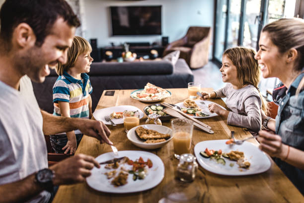 Young happy family talking while having lunch at dining table. Happy family communicating during lunch time in dining room. Focus is on kids. dining table photos stock pictures, royalty-free photos & images
