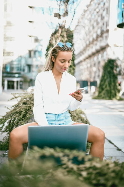istock Cute Blonde Female Using Portable Devices On a City Bench 1132282948