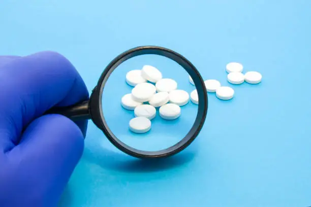Photo of Pharmacist or expert on pharmaceutical inspection identifies pills. Testing, verification and determining pharmaceutical counterfeiting or fakes of medicines and medicinal substance quality concept