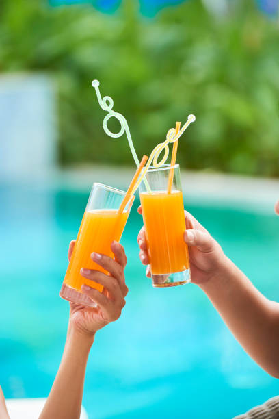 Close-up of young couple holding glasses with fresh orange juice and toasting outdoors in summer day