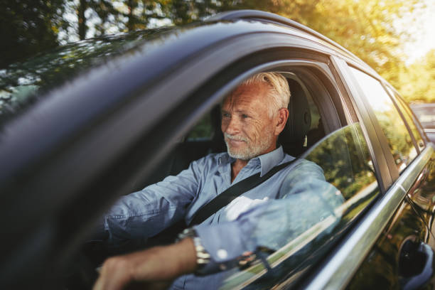 Smiling senior man driving on a tree lined country road stock photo