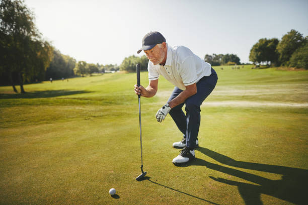 Senior golfer planning his putt on a golf green Sporty senior man crouching on a green planning his putt while enjoying a round of golf on a sunny day squatting position photos stock pictures, royalty-free photos & images