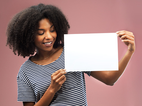 Studio shot of an attractive young woman holding a blank placard against a pink background