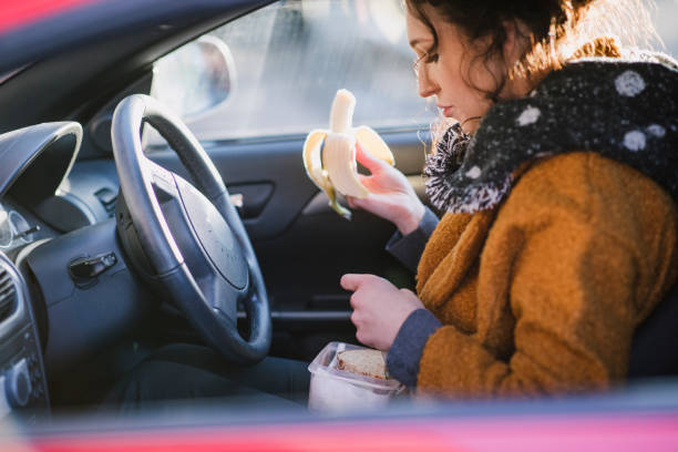 Quick Car Lunch Young businesswoman is sitting in the driver's seat of her car eating a banana. instant food stock pictures, royalty-free photos & images