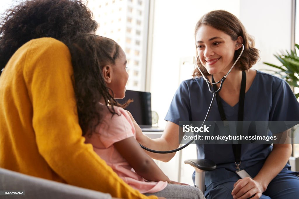 Mujer pediatra vistiendo Scrubs escuchando a las niñas pecho con estetoscopio en la oficina del hospital - Foto de stock de Personal de enfermería libre de derechos