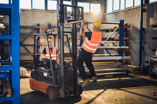 Manual worker having fun while exercising pull ups on a forklift in industrial building.