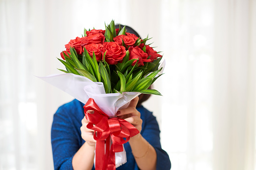 Portrait of woman holding big bouquet of red roses with big red bow in front of her face isolated on white background